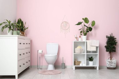 Tuvalet klozeti, raf ünitesi ve çekmeceler tuvaletteki pembe duvarın yanında.