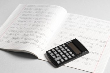 Gri arkaplanda el yazısıyla yazılmış matematik formülleri ve hesap makinesi olan metin kitabı