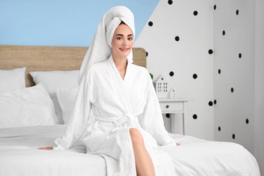 Duştan sonra havluyla bornozlu genç bir kadın evde yatakta oturuyor.