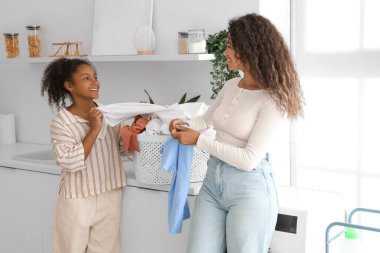 Afro-Amerikalı kadın ve kızı evde çamaşır yıkıyorlar.