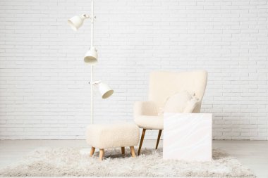 Koltuk, puf, yer lambası ve beyaz tuğla duvarın yanındaki oda.