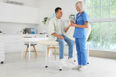 Dişilik endokrinoloğu elinde tükenmez kalemle klinikteki erkek hastanın kan şekerini ölçüyor.