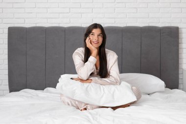 Genç ve güzel bir kadın yastıkla yatakta oturuyor.