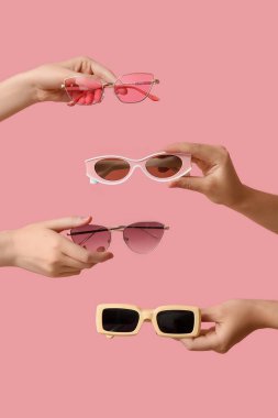 Pembe arka planda birçok şık güneş gözlüklü kadın elleri