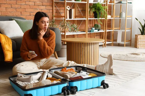 Cep telefonlu genç bir kadın kışlık kıyafetlerini bavuluna koyup eve gidiyor.