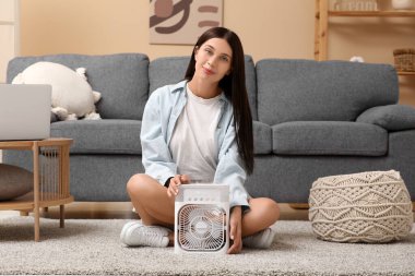 Oturma odasında nemlendirici ile taşınabilir vantilatörün yanında oturan güzel genç bir kadın.