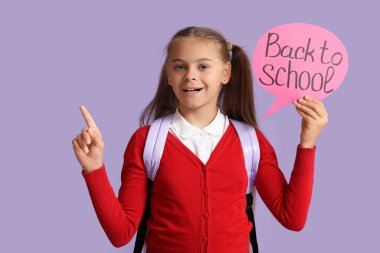 Okul üniformalı, elinde konuşma balonuyla okula geri dönen ve leylak arkaplanındaki bir şeye işaret eden sevimli küçük bir kız.