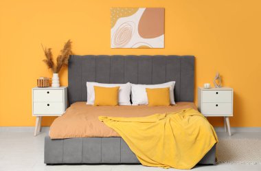 Rahat yataklı, komodinli güzel bir yatak odası, otların resmi ve vazosu.