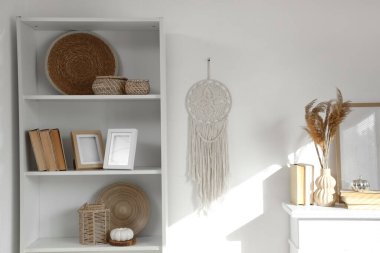 Beyaz duvarın yanında balkabağı, hasır dekorlu raf ünitesi, kitaplar ve fotoğraf çerçeveleri.