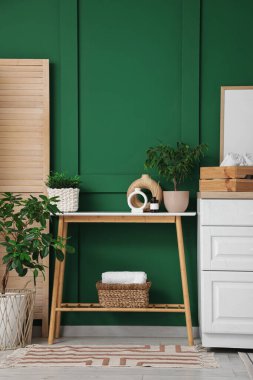 Ahşap bank, çekmece sandığı ve yeşil duvarın yanındaki katlı ekran.