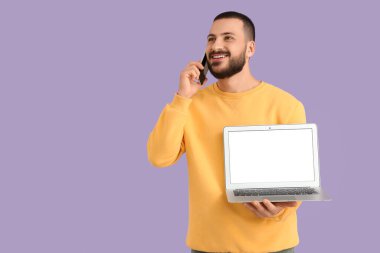 Laptoplu genç adam cep telefonuyla konuşuyor.