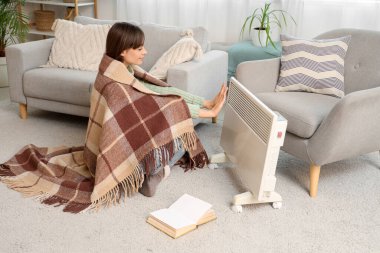 Evinde elektrikli konteyner ısıtıcısının yanında sıcak ekoseli elleri olan genç bir kadın.