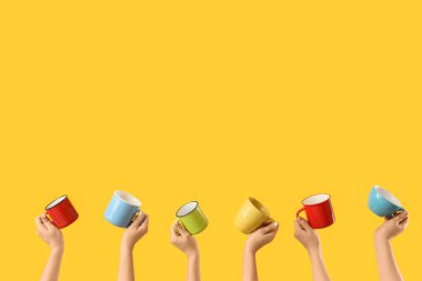Sarı arka planda farklı kupaları olan kadın elleri.