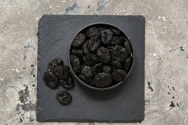 Gri arkaplanda kuru erik olan siyah kase.