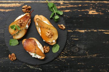 Siyah ahşap zemin üzerinde ricotta peynirli, cevizli ve naneli armut bruschetta.