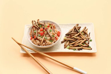 Bir kase kızarmış kurtlu pilav ve turuncu arka planda yeşil soğan.