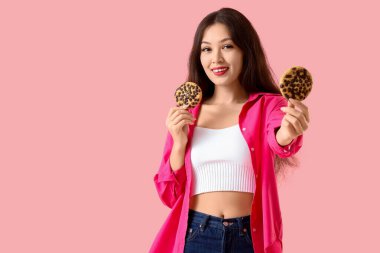 Pembe arka planda kurabiyeleri olan genç Asyalı kadın.