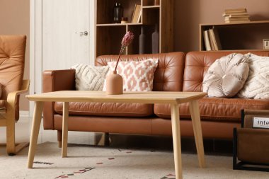 Vazoda tropik çiçekli kahve masası ve oturma odasında kahverengi kanepe.