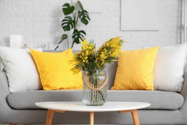 Oturma odasındaki masada mimoza çiçekli vazo.