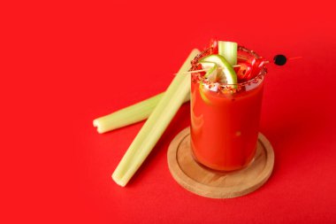 Kırmızı arka planda kırmızı biberli ve kerevizli bir bardak Bloody Mary kokteyli.