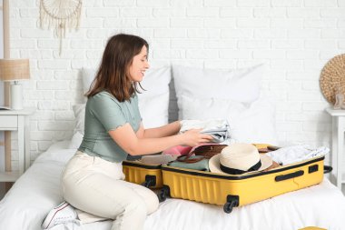 Güzel genç bir kadın, açık otel odasında bavulunu giysileriyle açıyor.