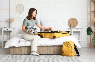 Güzel genç bir kadın, açık otel odasında bavulunu giysileriyle açıyor.