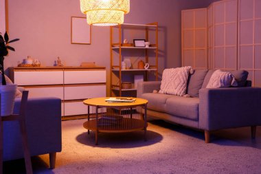 Geceleri kanepeleri, masası ve parlayan lambası olan oturma odasının içinde.