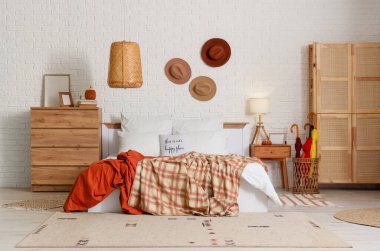 Modern yatak odasının içinde rahat yatak odası, şifonyer ve beyaz tuğla duvarın yanında birçok dekor unsuru var.