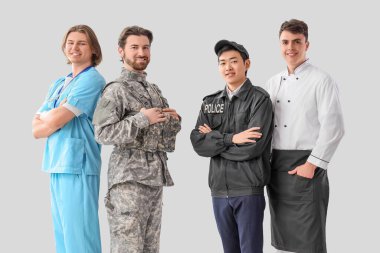 Aydınlık arkaplanda farklı mesleklerden üniformalı bir grup genç adam.