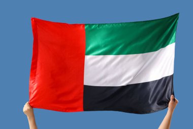 Mavi arka planda BAE bayrağı olan kadın eller