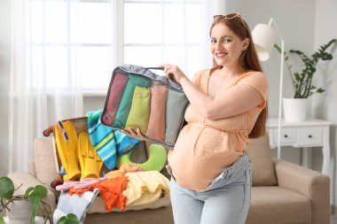 Genç hamile bir kadın, çantasını elbiseleriyle birlikte evde tutuyor.