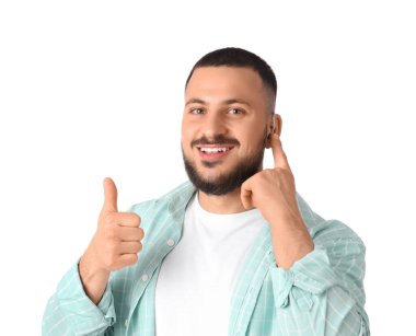 İşitme cihazı olan genç adam beyaz arka planda baş parmak gösteriyor.