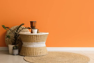 Davullu kahve masası, bitkiler ve puf, turuncu duvarın yanında.