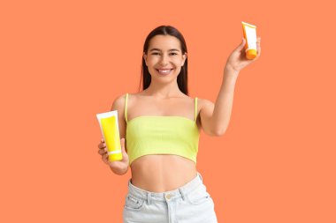 Turuncu arka planda güneş kremleri olan genç bir kadın.