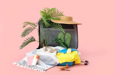 Kulaklıklı bavul, ev bitkisi ve pembe arka planda plaj aksesuarları.