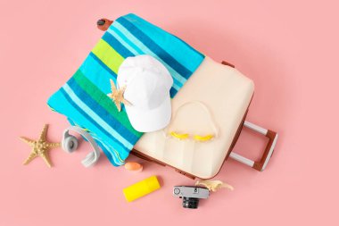 İçinde deniz yıldızları, kulaklıklar ve pembe arka planda plaj aksesuarları olan bavul.
