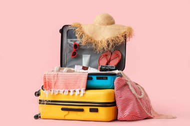 Fotoğraf makineli bavullar ve pembe arka planda plaj aksesuarları.