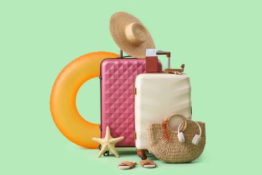Bavullar, şişme yüzük ve yeşil arka planda plaj aksesuarları.