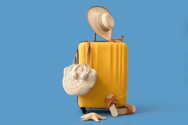 Bavul, denizyıldızı, kulaklık ve mavi arka planda plaj aksesuarları.