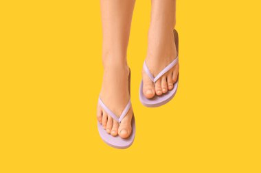 Sarı arka planda leylak rengi terlikler giyen genç kadınların bacakları.