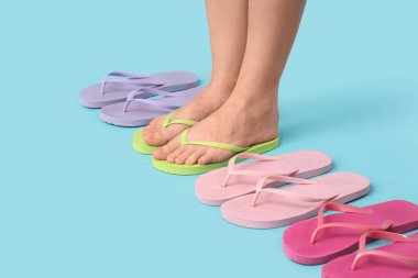 Mavi arka planda farklı tarz parmak arası terlikleri olan genç bir kadının bacakları.