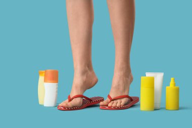 Kırmızı parmak arası terlik ve mavi arka planda güneş kremi sürmüş genç bir kadının bacakları.