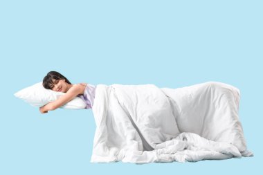 Mavi arka planda, yastıklı ve battaniyeli genç bir kadın.