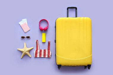 Bavul, mayo ve aksesuarlar leylak arka planda.