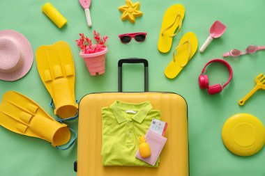 Yeşil arka planda bavullu ve plaj aksesuarlı kompozisyon, yakın plan.