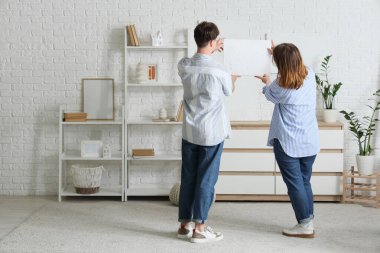 Genç bir çift eve resim asıyor.