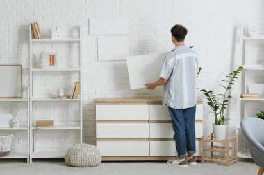 Evdeki beyaz tuğlalı duvara resim asan genç adam.