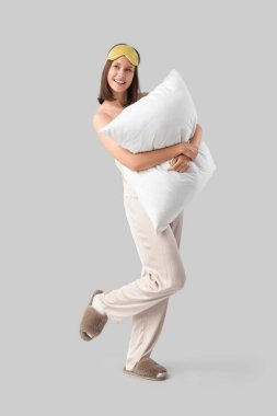 Hafif arka planda yumuşak yastıklı pijamalı genç bir kadın.