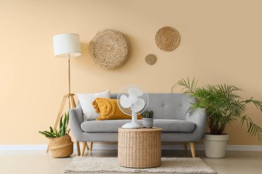 Oturma odasının içinde kanepe, bitki ve vantilatör var.