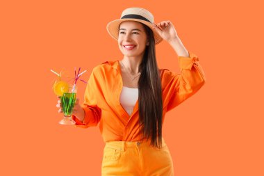Turuncu arka planda kokteyli olan yaz şapkalı şık bir genç kadın.